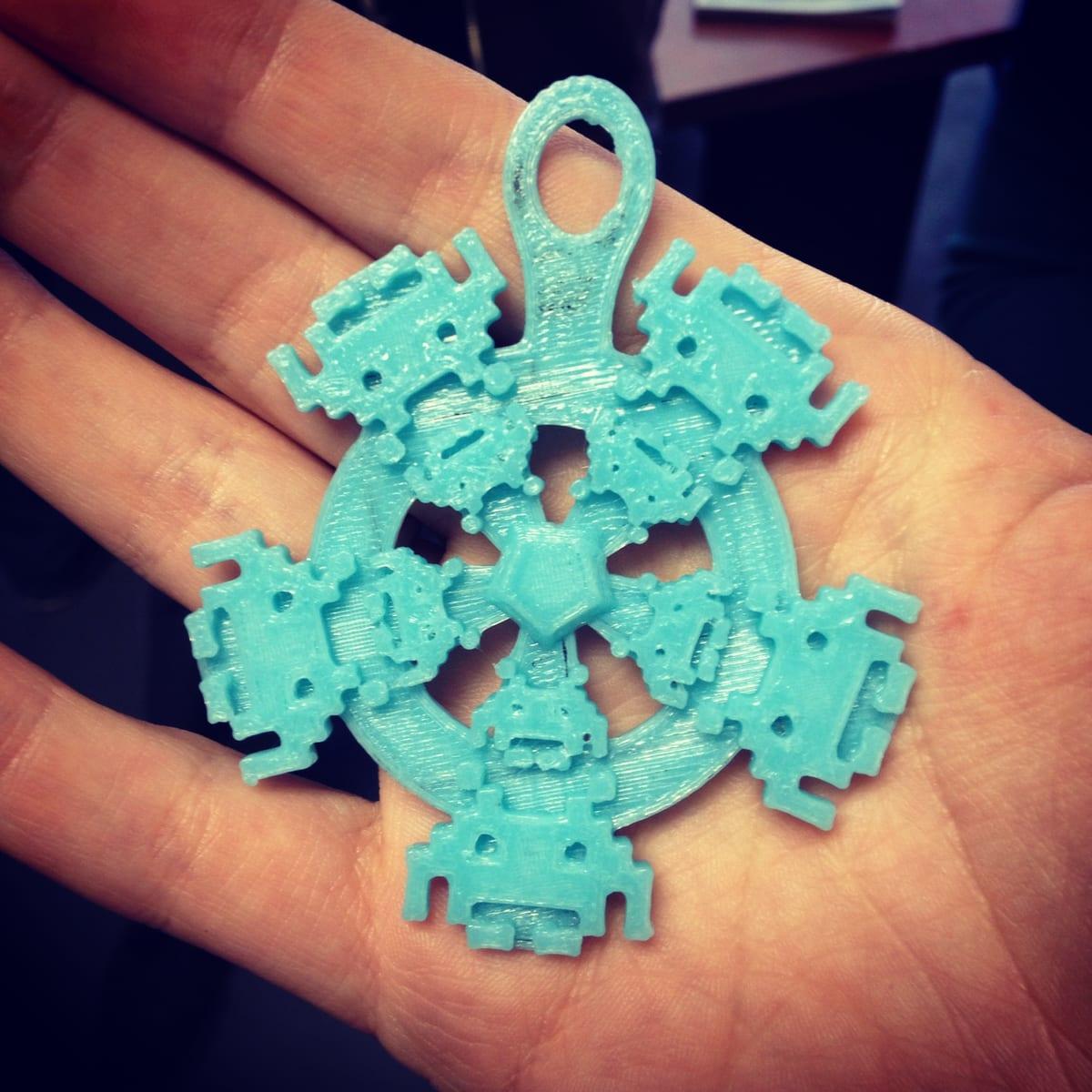 A hand holding a light blue 3D printed snowflake ornament made of pixel-art figures, with visible print layer lines
