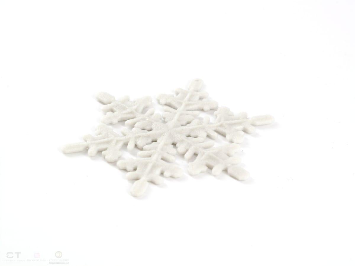 A white 3D printed snowflake ornament with fine six-fold arms, photographed flat on a white background
