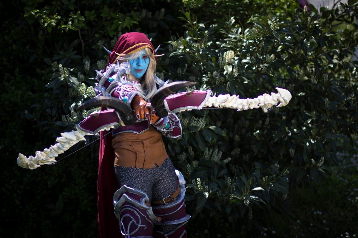 A blue-skinned fantasy cosplayer in shoulder armour and bracers holding a large bone bow