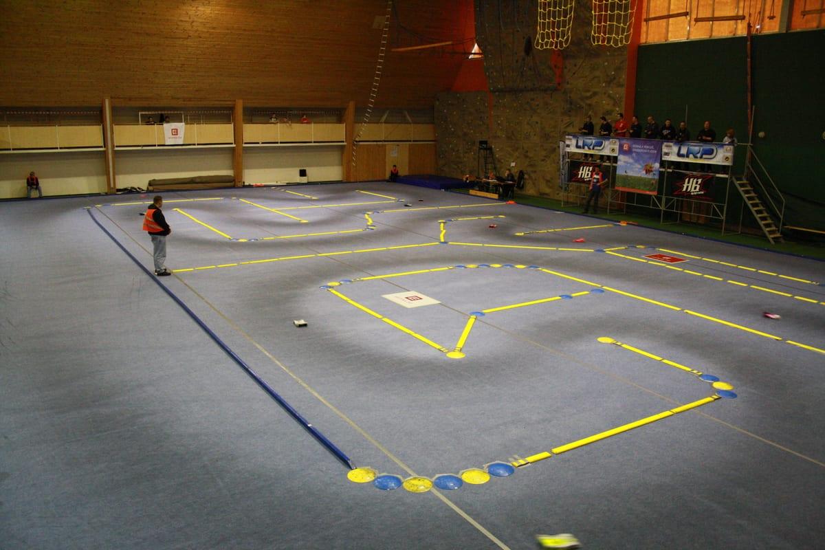 Indoor radio-control car racing track laid out in a gymnasium with barriers and marshals