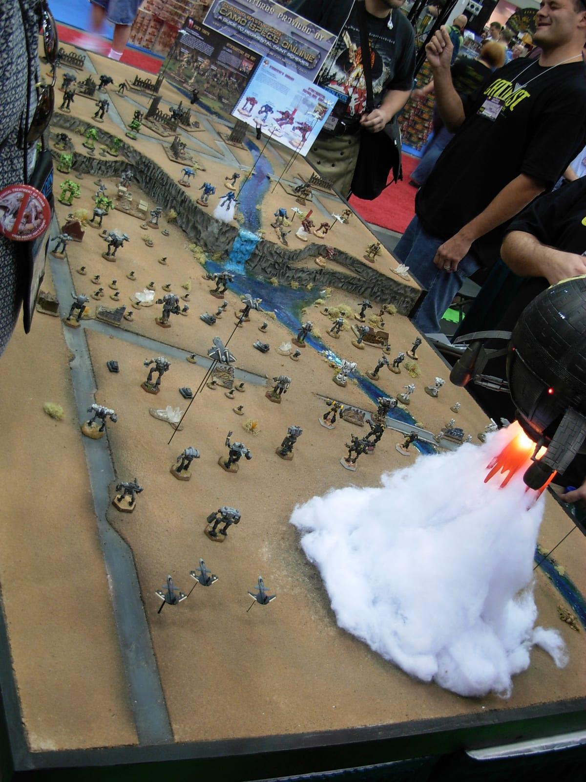 A sci-fi wargaming board with a rocky ravine and stream, covered with painted mech miniatures