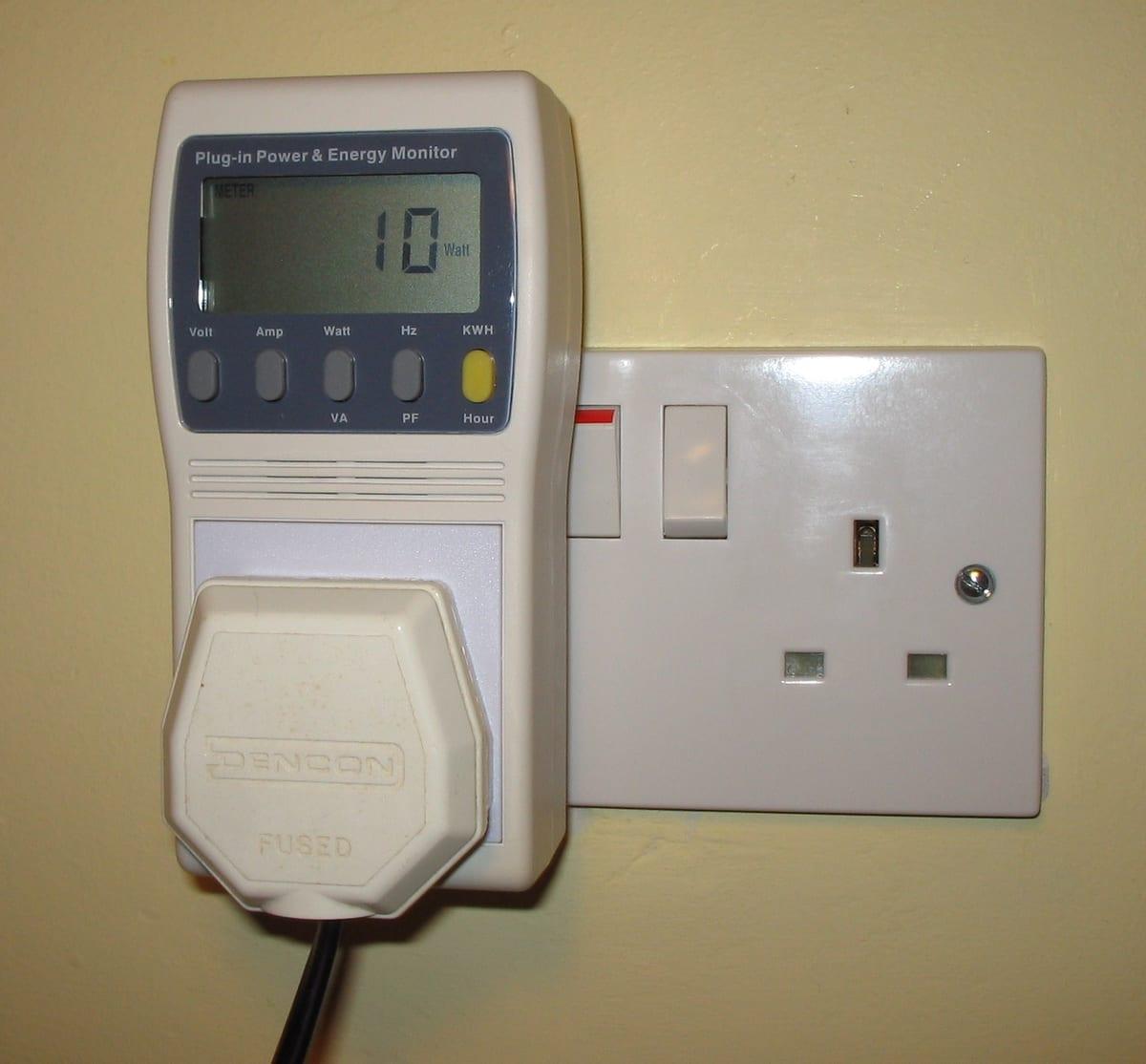 A plug-in power and energy monitor in a mains wall socket showing a digital wattage readout