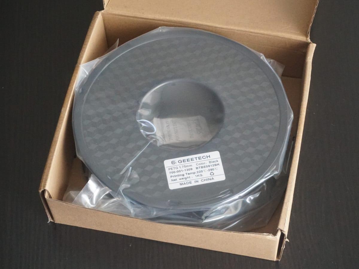 A one-kilogram spool of black PETG filament in its packaging with the net weight label visible