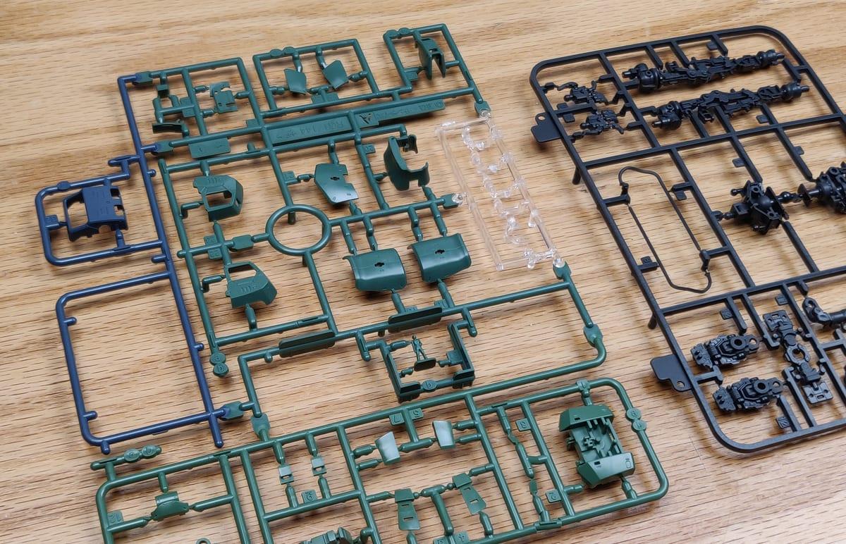 Green, black and blue injection-moulded plastic model kit sprues laid out on a wooden table, each holding dozens of small parts