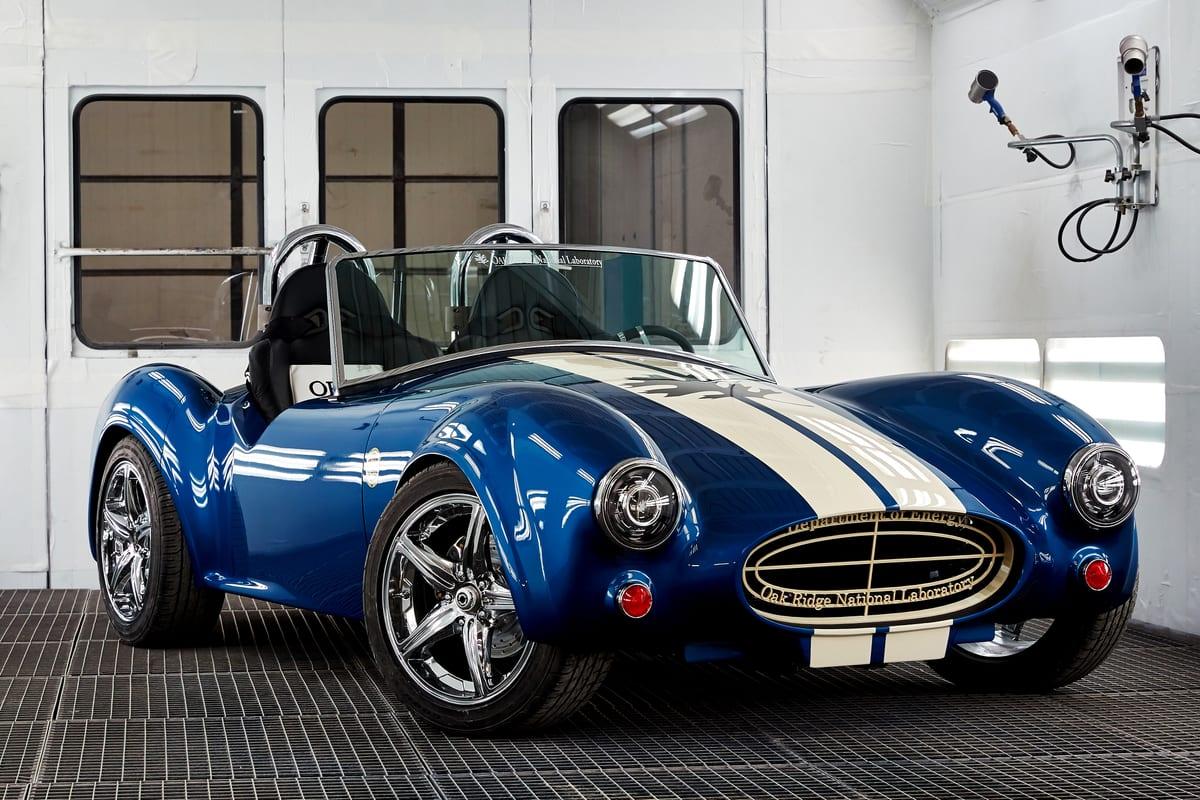 A blue and white Shelby Cobra replica whose body was produced by large-format additive manufacturing, displayed indoors