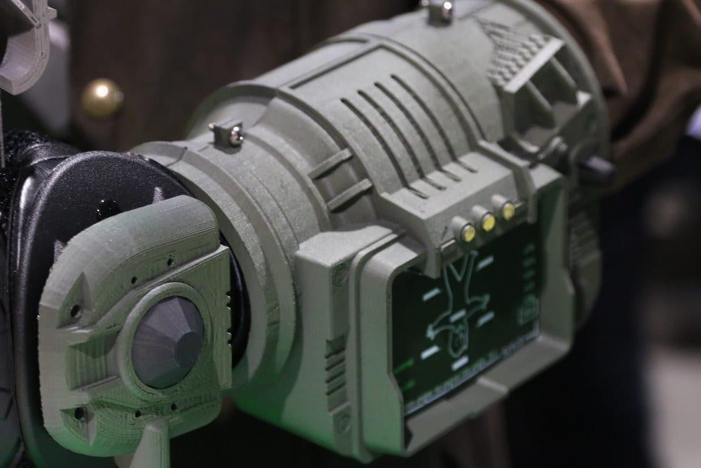 A 3D printed sci-fi forearm gauntlet prop worn on a cosplayer's arm, its FDM layer lines clearly visible across the grey plastic panels, lens housing and screen bezel
