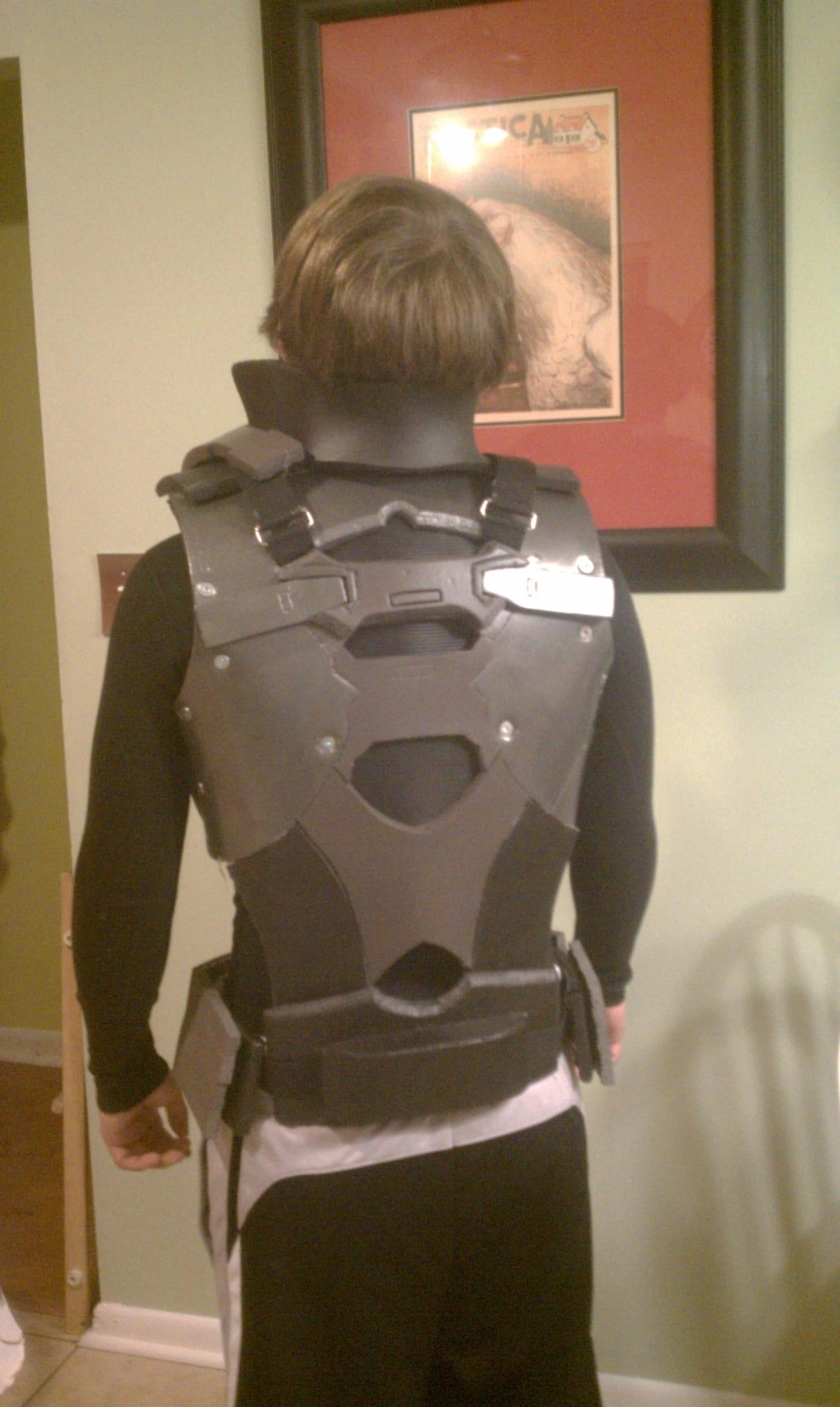 A person seen from behind wearing a grey costume torso harness built from shaped and sealed EVA foam panels over a black base layer