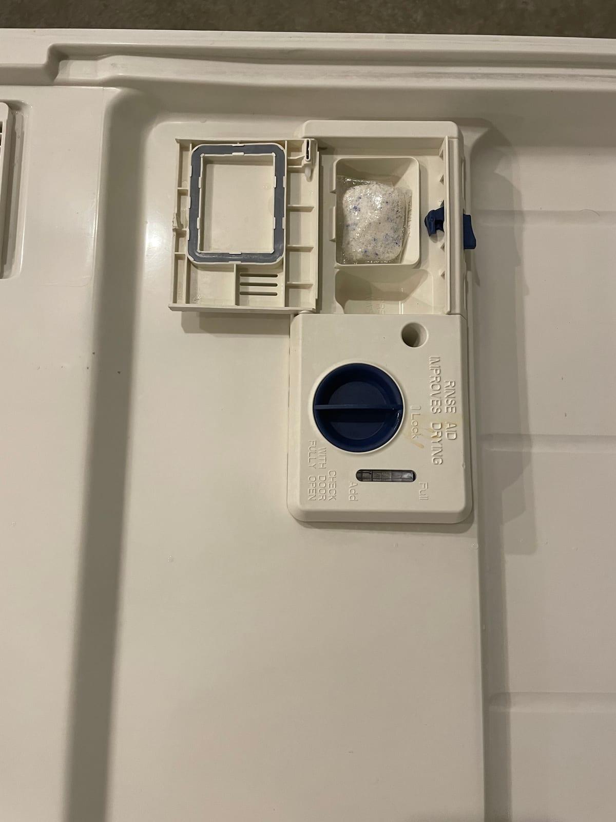 The inner door panel of a dishwasher showing the detergent compartment, its hinged lid and the rinse aid cap