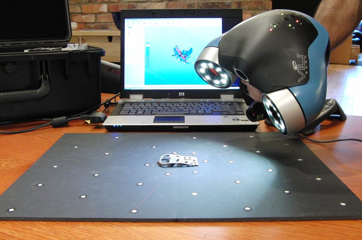 A person using a handheld 3D scanner to capture the shape of an object on a workbench