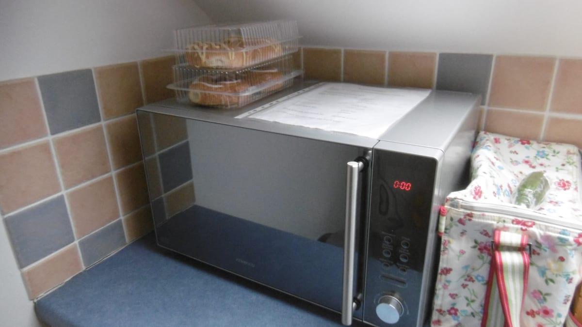 Stainless microwave oven fitted into a tiled kitchen alcove with a vertical tubular bar handle on the door