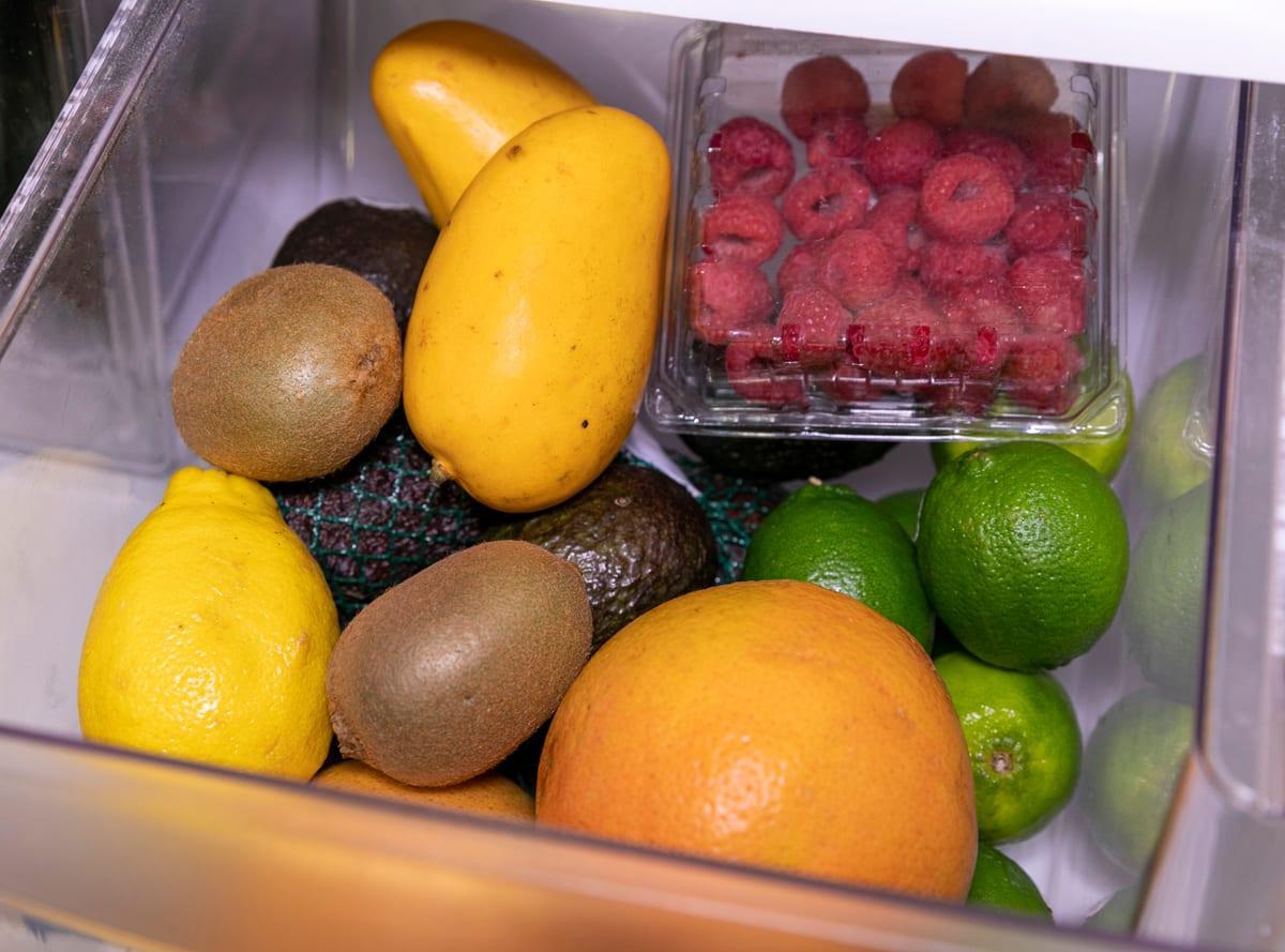 Loose fruit including citrus, kiwi and avocados inside a clear refrigerator crisper drawer