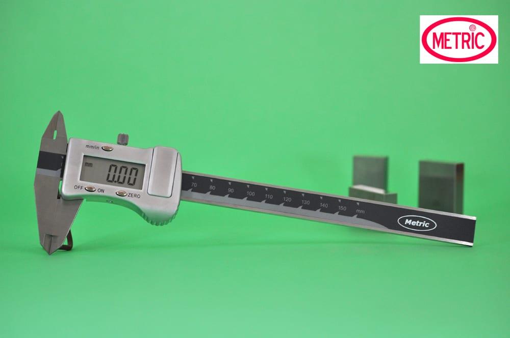 A digital caliper lying on a green background with its jaws closed and the display zeroed at 0.00 mm