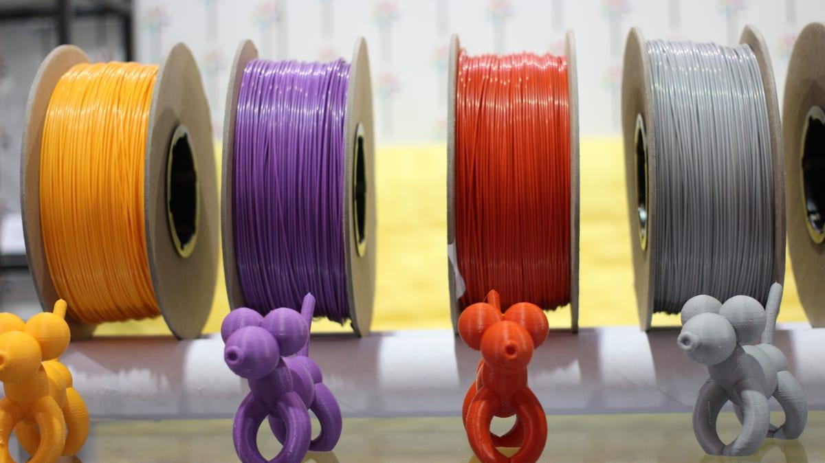 Spools of 3D printing filament in four colours on a display, each with a small printed sample figure in front of it