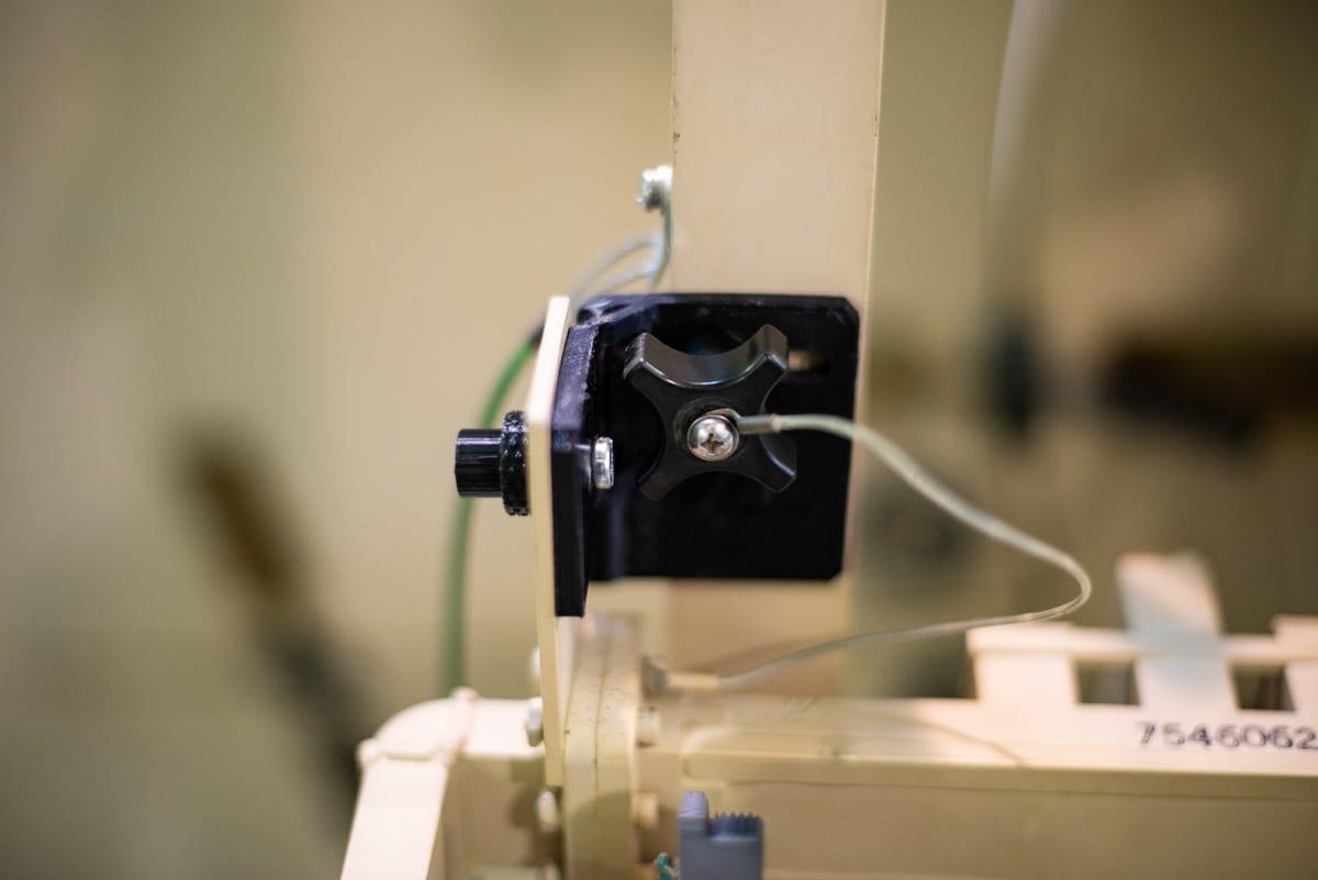 Black 3D printed nylon bracket bolted in place, clamping a knob and cable on an equipment frame