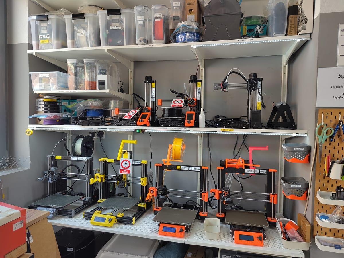 Rack of desktop 3D printers stacked on shelving in a hackerspace print farm