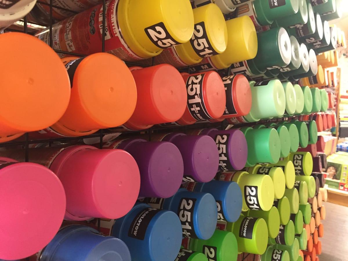 A shop display rack packed with aerosol spray paint cans, seen end-on so only the coloured caps are visible