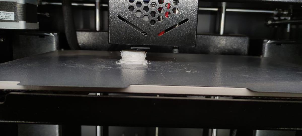 Close-up of the first layers of a small white part being extruded onto a 3D printer build plate