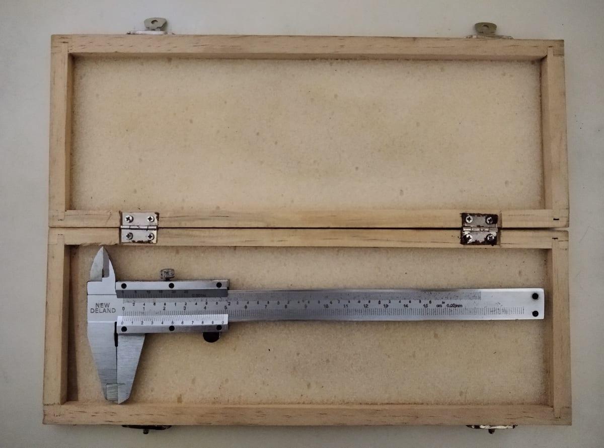 A stainless steel vernier caliper lying open in its hinged wooden storage case