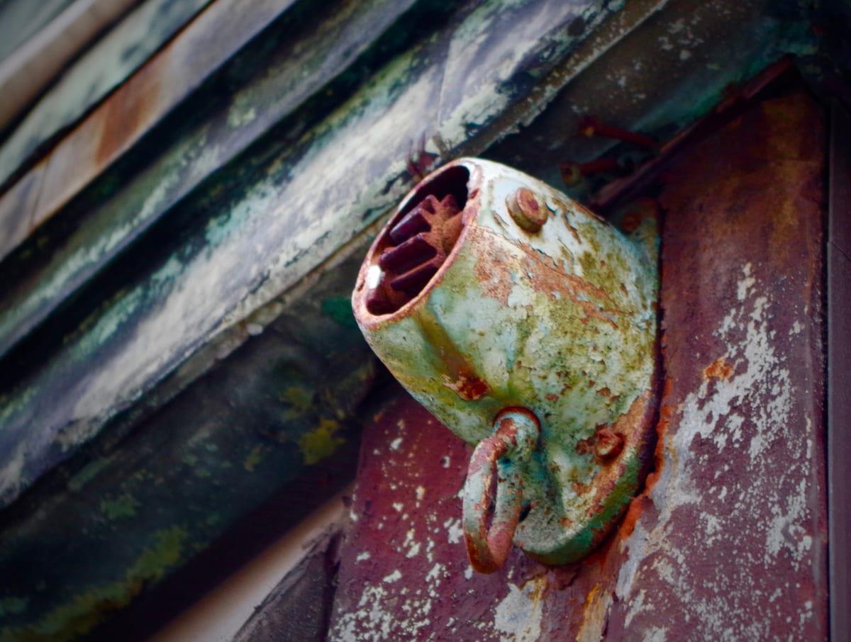 Weathered green painted metal gear housing for a hand-cranked window awning, with the splined drive socket visible