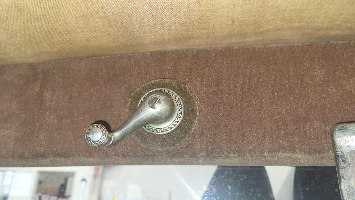 Metal crank handle with a rotating knob mounted on an upholstered panel through a decorative escutcheon plate