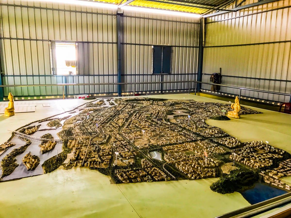 An enormous physical city masterplan model filling the floor of a warehouse, showing thousands of small buildings, road networks, waterways and green space