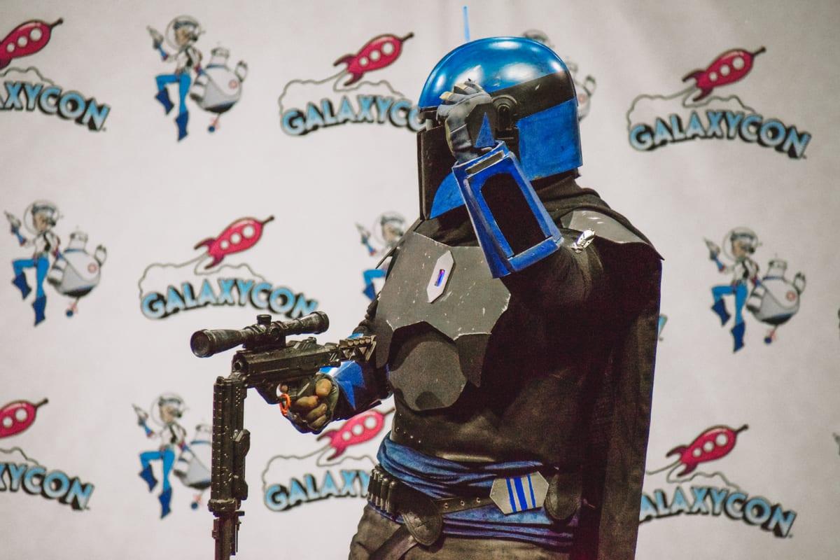 A closer view of a Mandalorian-style cosplayer showing the helmet shape, T-visor and shoulder armour