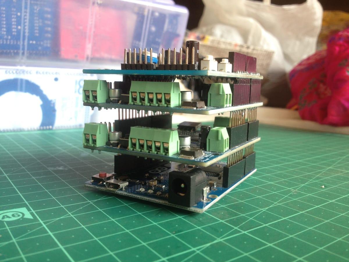 An Arduino board with three expansion shields stacked on top of it, viewed from the side so the pin headers, screw terminals and total assembled height are visible