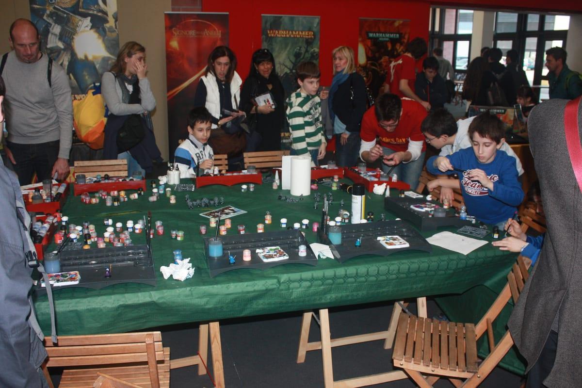 People seated around a long table painting small tabletop miniatures with pots of paint and brushes laid out