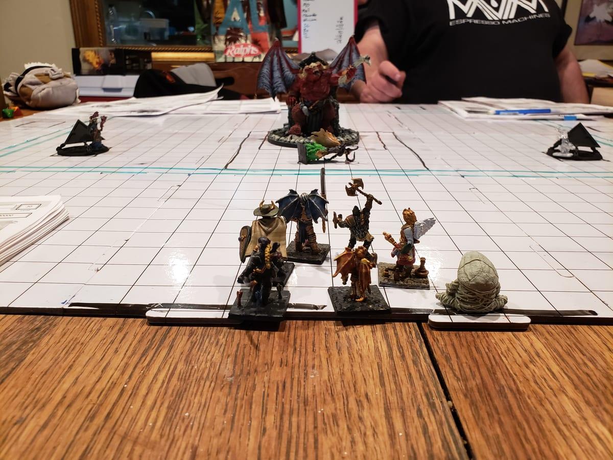 Painted tabletop miniatures arranged on a gridded battle mat during a roleplaying session